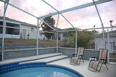 Empty chairs by swimming pool against building
