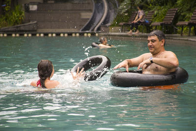 Daughter and father playing with black inflatable ring in swimming pool