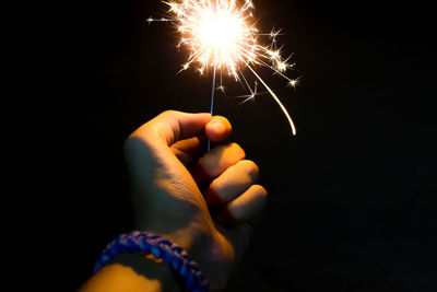 Cropped hand of person holding sparkler at night