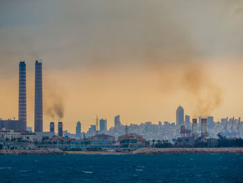 Sea and buildings in city at sunset