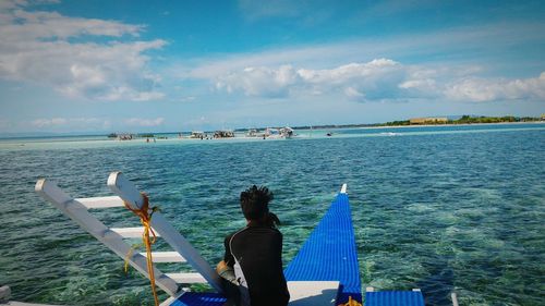 Rear view of man sitting on boat in sea against sky