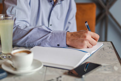 Midsection of businessman writing in diary at cafe