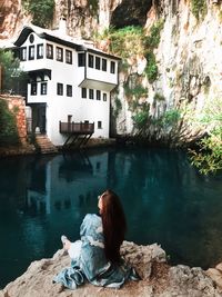 Rear view of woman sitting on rock by lake