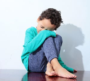 Cute boy sitting against wall stock photo