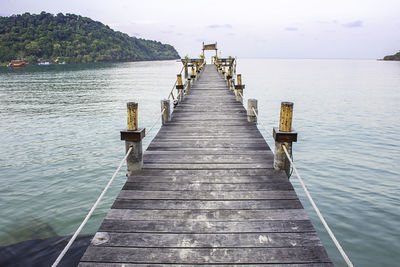 Wooden jetty leading to pier over sea against sky