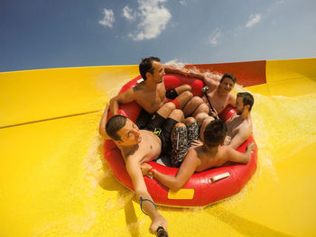 Friends sitting in inflatable ring on slide against sky
