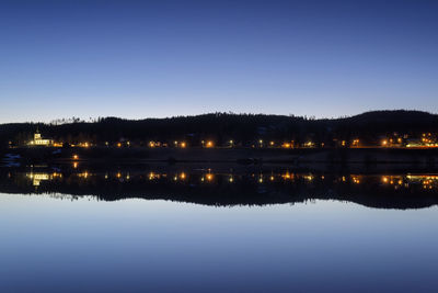 Reflection of illuminated trees in lake against clear blue sky