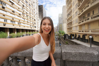 Portrait of young woman standing against buildings