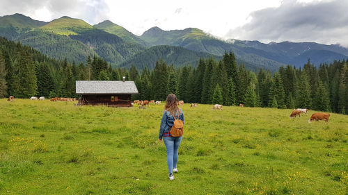 Rear view of woman walking on grass with mountains in background