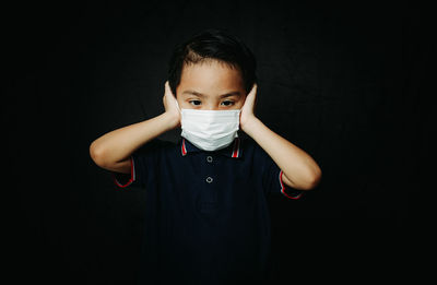 Portrait of boy standing against black background