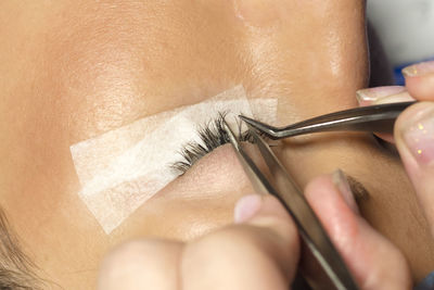 Close-up of beautician applying false eyelash to customer