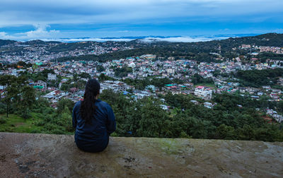 Young girl watching downtown city view with dramatic cloudy sky at evening from mountain top