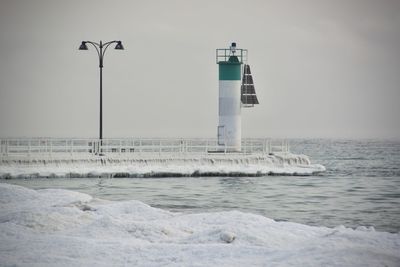 Lighthouse by sea against clear sky