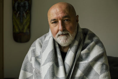 Portrait of serious mature man wrapped in blanket at home
