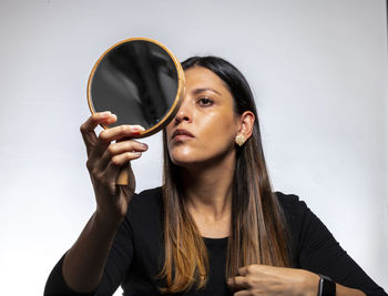 Portrait of young woman holding camera against wall