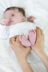 Cropped hands of mother holding toddler daughter legs on bed