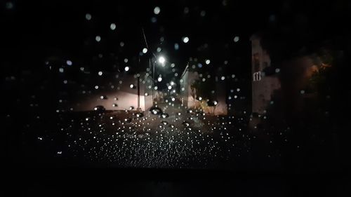 Illuminated city seen through wet window at night