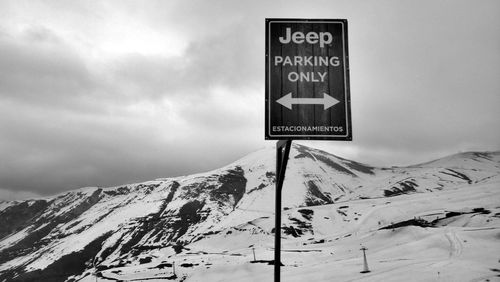 Information sign on snow covered mountain against sky