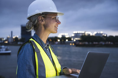 Thoughtful female professional smiling while holding laptop