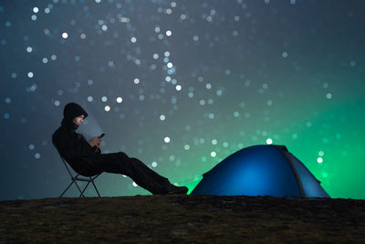 Side view of man using mobile phone while sitting on field at night