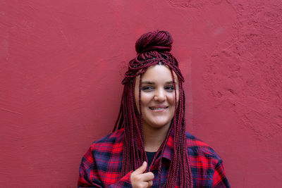 Portrait of young woman with dreadlocks standing against bright red wall