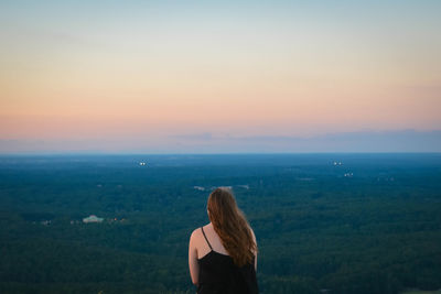 Rear view of woman standing over landscape against sky during sunset