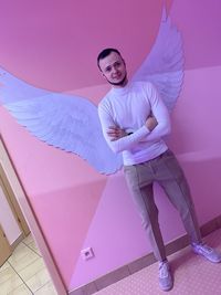 Portrait of young man standing against pink wall