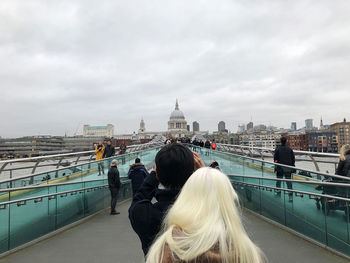 Rear view of women on bridge against cloudy sky