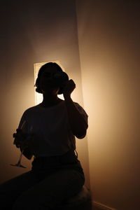 Rear view of silhouette man sitting on wall at home