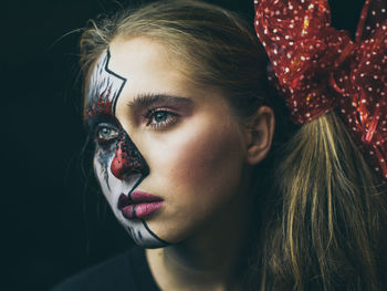 Close-up of woman with painted face against black background