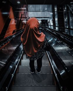 Rear view of woman wearing hijab standing on escalator