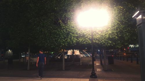 Woman walking on illuminated street light in city at night