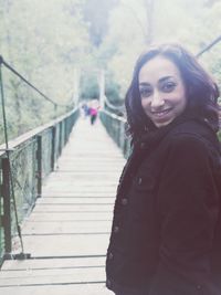 Portrait of smiling young woman standing on footbridge