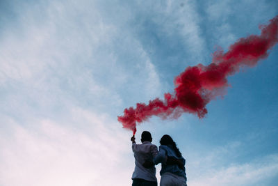 Rear view of man holding distress flare while embracing woman against sky