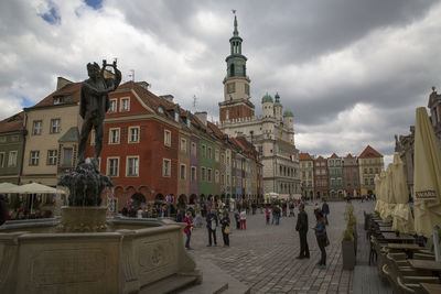 People at city square against cloudy sky