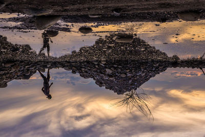 Upside down image of man reflecting on puddle during sunset