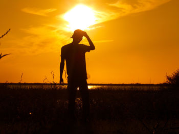 Silhouette man standing on field against sky during sunset