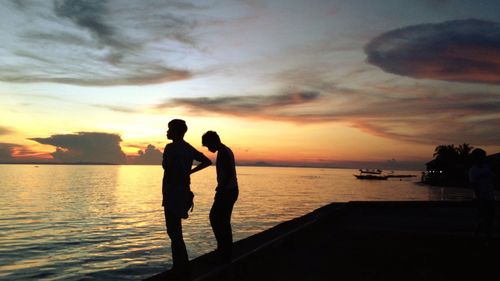 Silhouette couple standing on beach against sky during sunset