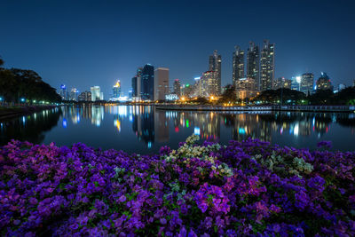 Scenic view of river by illuminated city against clear blue sky