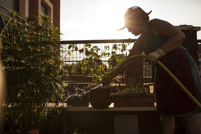 Side view of mature woman gardener watering her garden with hose