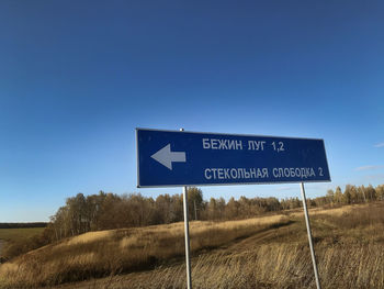 Road sign on field against clear blue sky