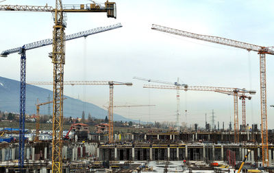 Cranes at construction site in city against sky