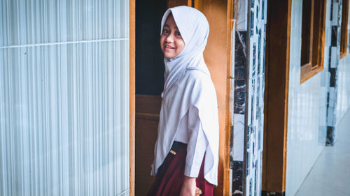 Portrait of young woman standing against door