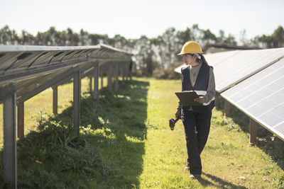 Female maintenance engineer examining solar panels while walking at power station