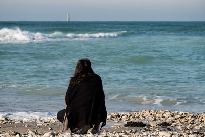 Rear view of woman standing on beach against clear sky