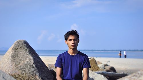 Man sitting by rocks at beach against sky