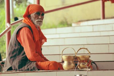 Portrait of sadhu with containers sitting on staircase