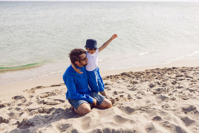 Dad and son in sunglasses play on the beach in summer in blue clothes while on vacation