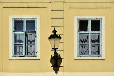 Two windows on yellow wall with lamp between