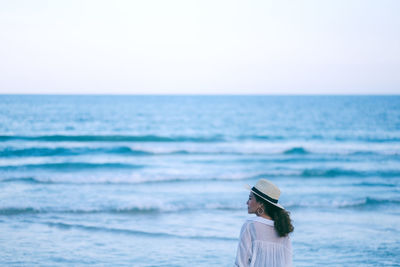 Rear view of woman looking away while standing by sea